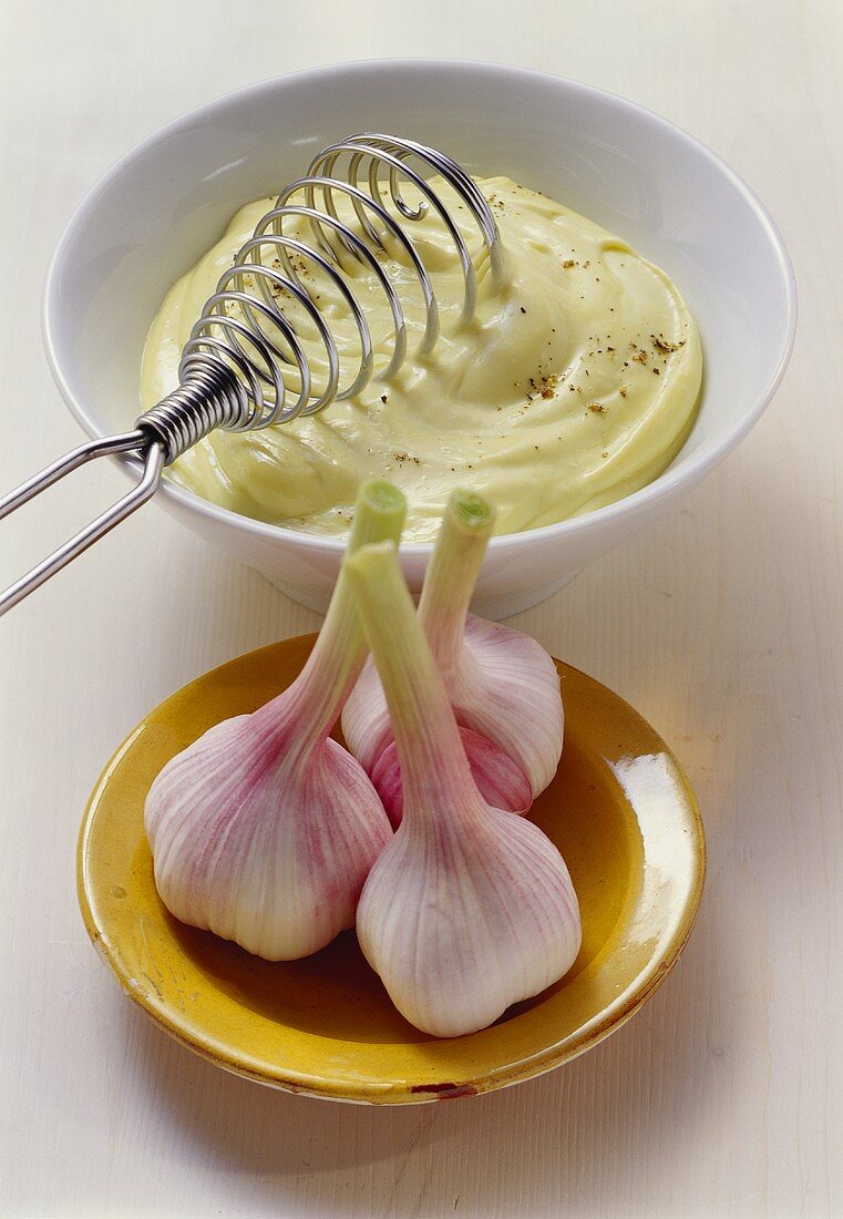 Bowl of aioli (garlic mayonnaise) & three garlic bulbs