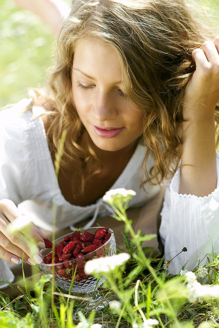 Young woman in grass with a bowl of wild strawberries