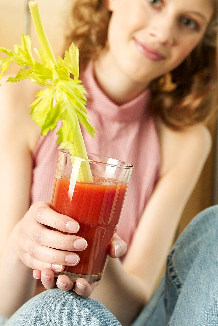 Frau hält Glas Tomatensaft, garniert mit Selleriestange