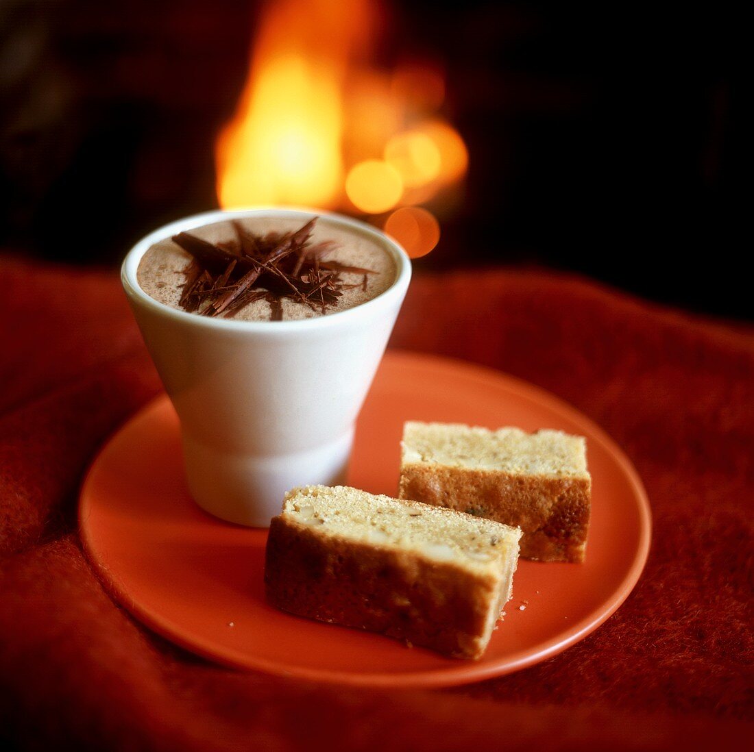 Beaker of hot chocolate & two pieces of nut cake by fireside