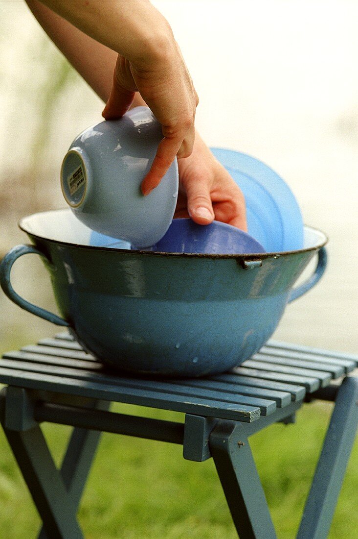Washing crockery in blue bowl on camping stool