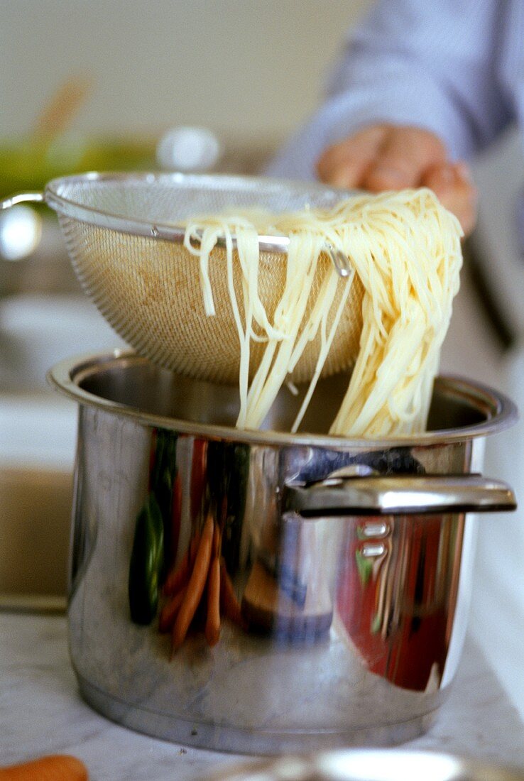 Cooked spaghetti in sieve over pan