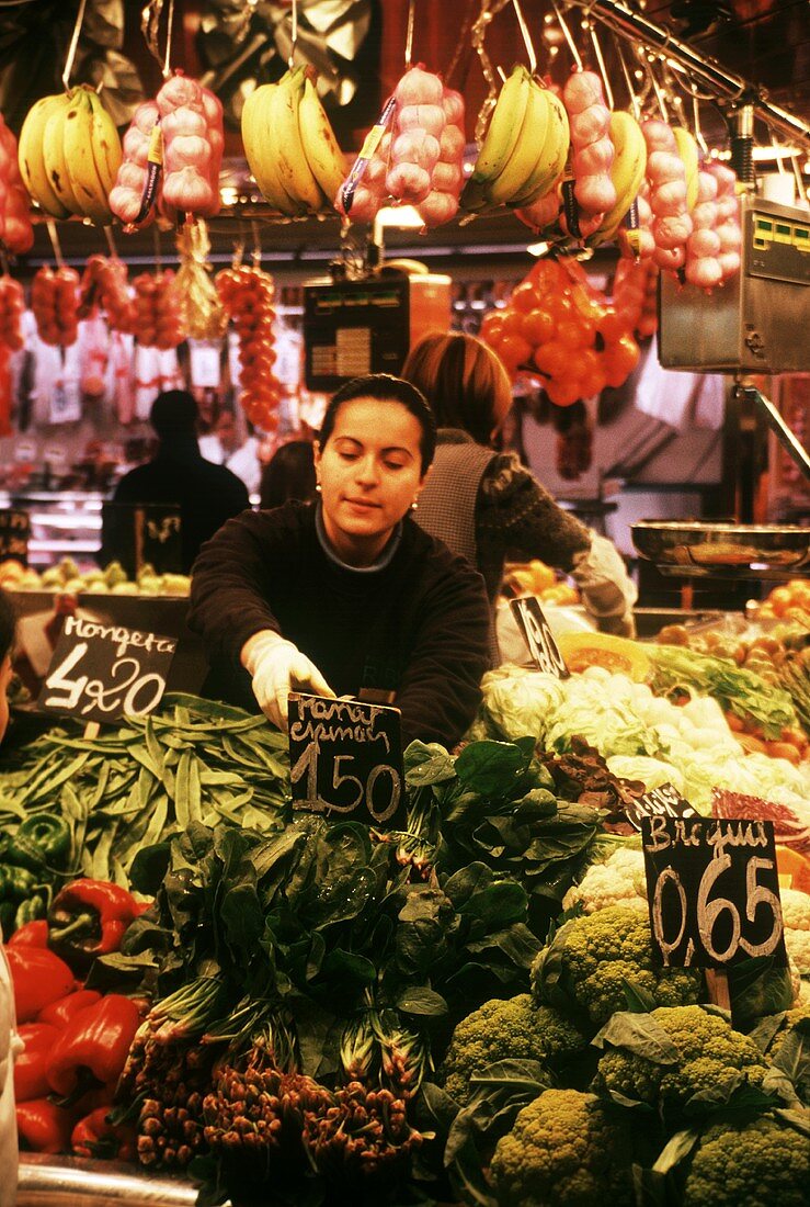 Woman selling vegetables at stall in the Boqueria in Barcelona
