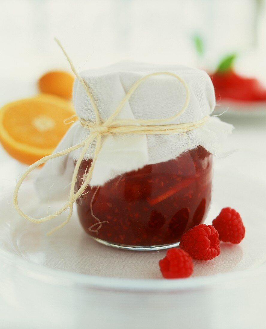 Jar of raspberry and orange jam, three raspberries beside it