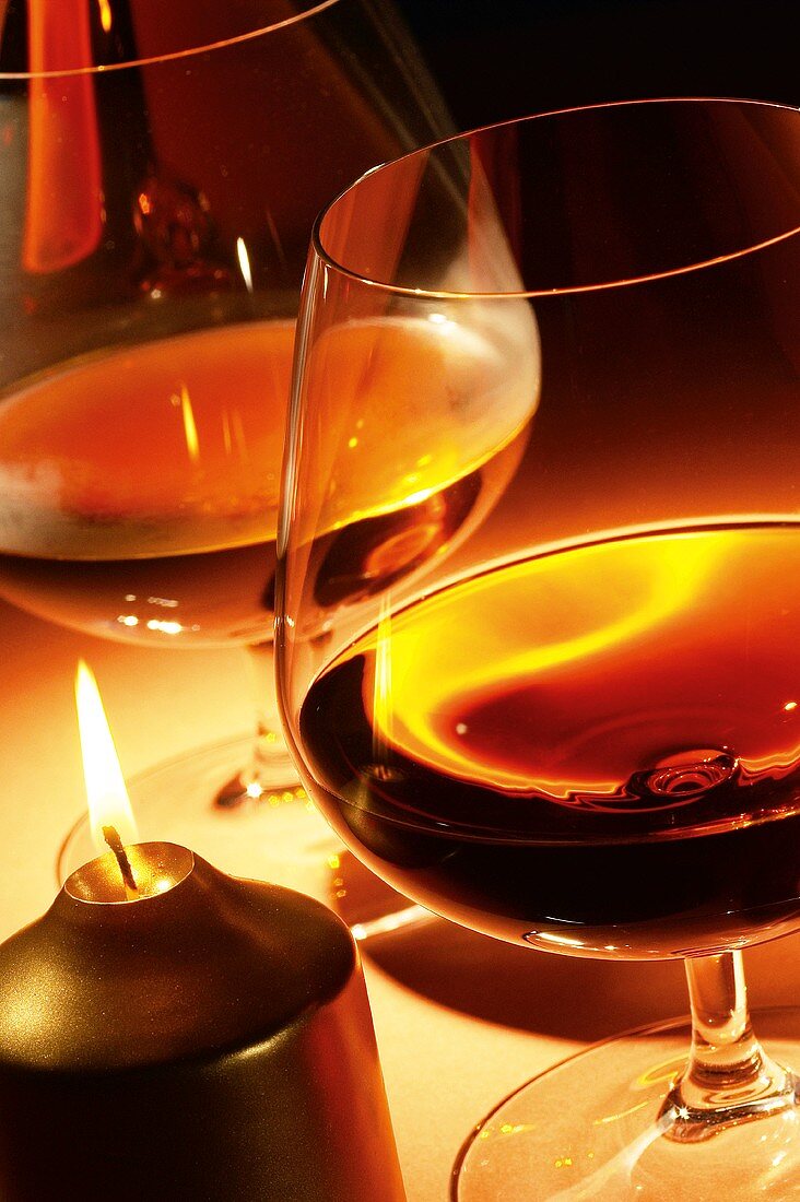 Brandy in Cognacschwenkern neben Kerze auf dem Tisch