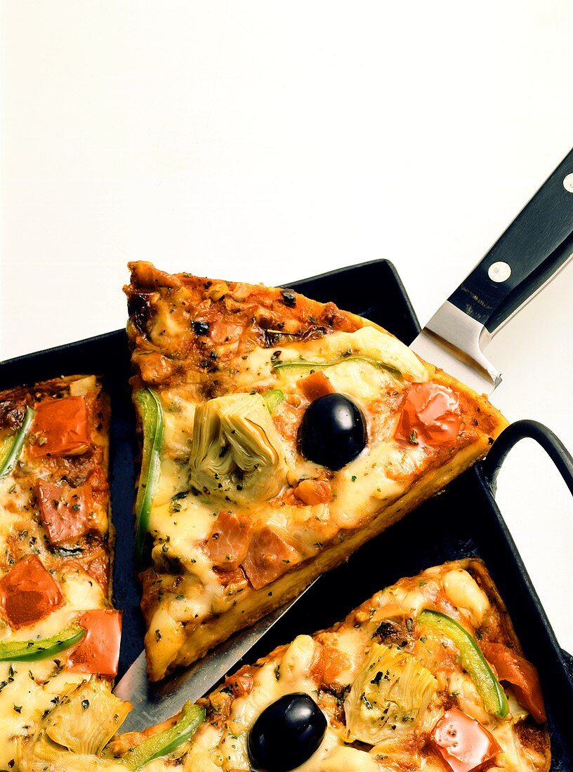 Gemüse-Schinken-Pizza auf Blech, ein Stück hochgehoben