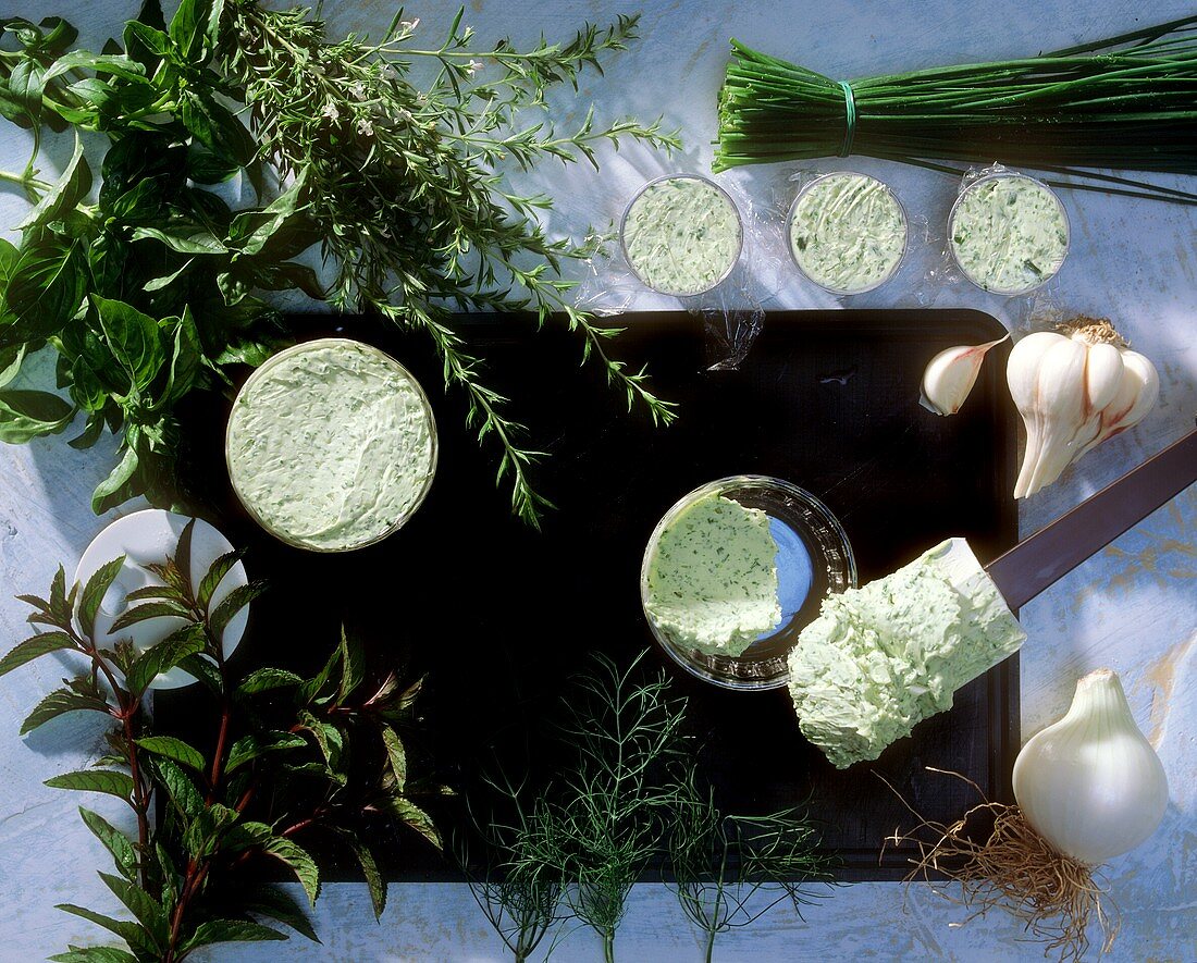 Several bowls of herb butter and various kinds of herbs