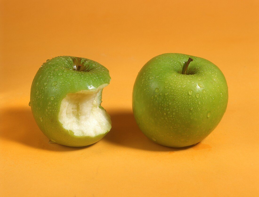 One whole Granny Smith apple and one with a bite taken