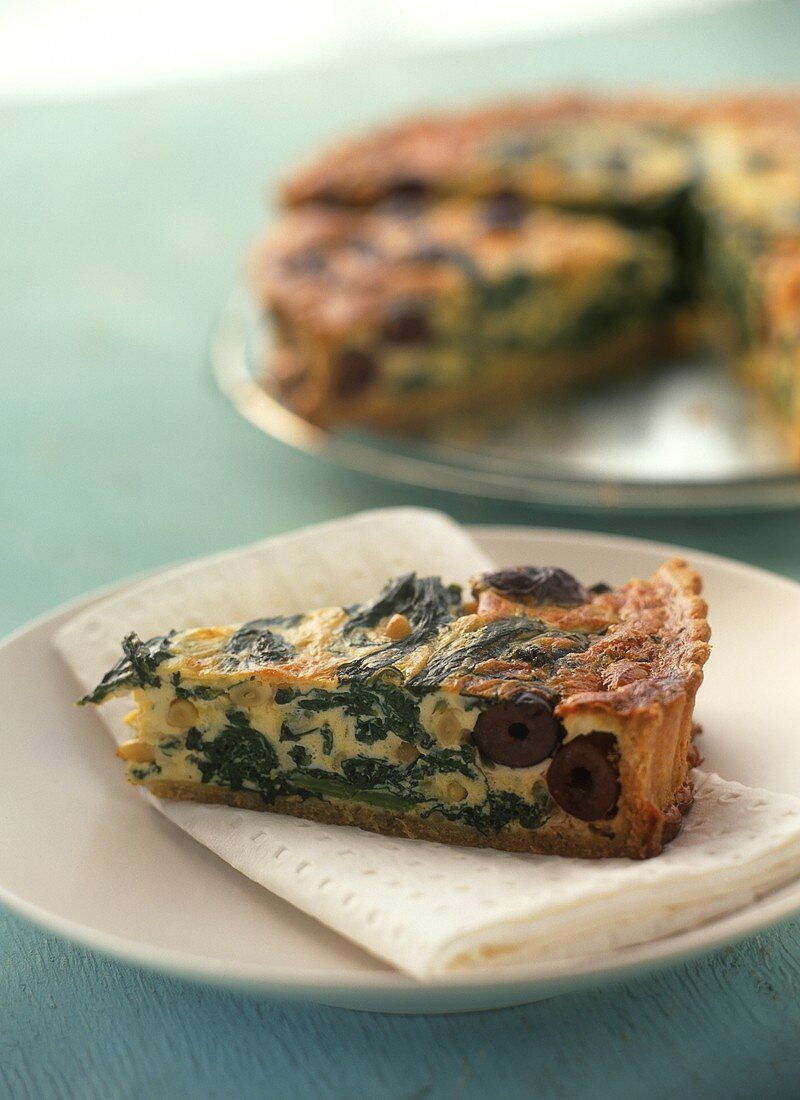 Piece of spinach and olive quiche with pine nuts