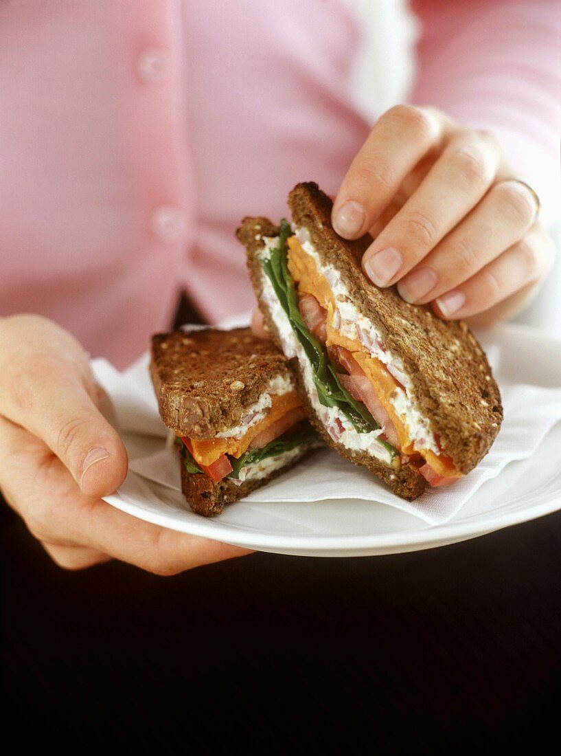 Hand hält Vollkornsandwich mit Süsskartoffeln, Salat, Ricotta