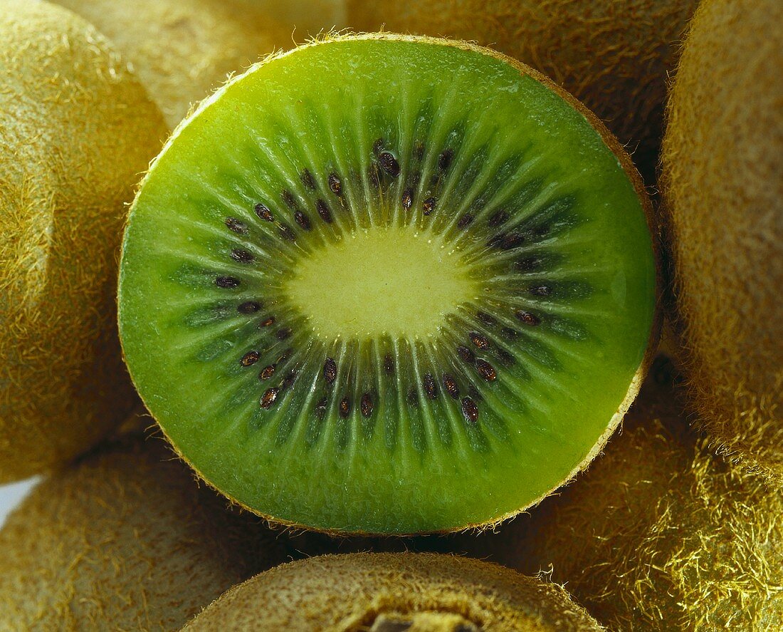 Half a kiwi fruit among whole fruits (close-up)