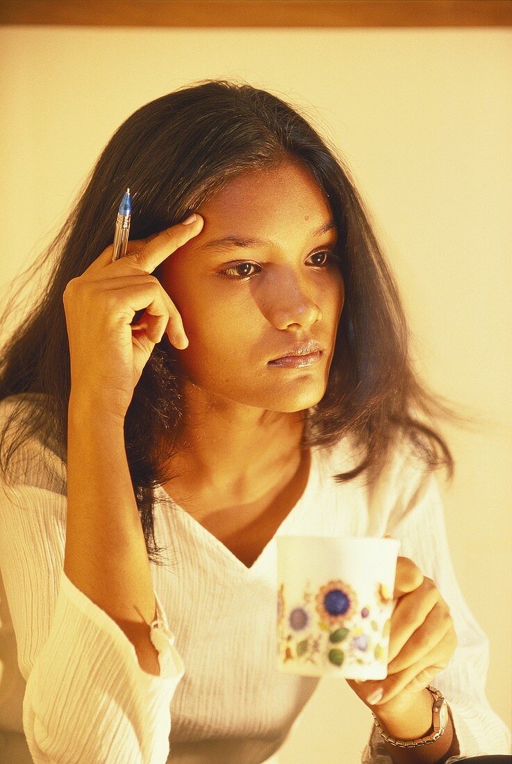 Pensive young woman, holding a cup in her hand