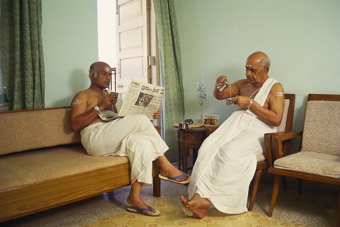 Two S. Indian men in white lungis drinking coffee