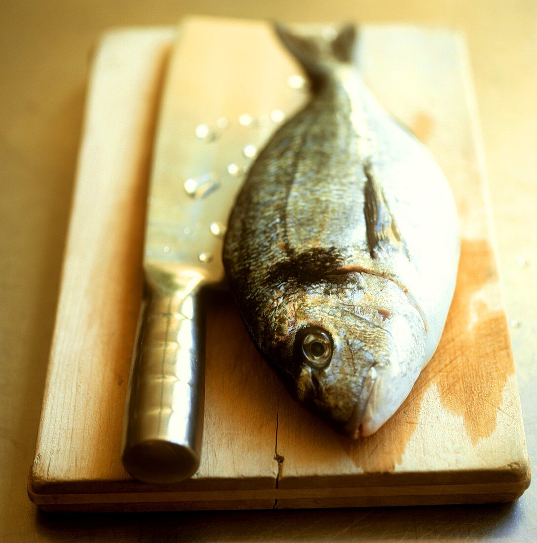 Gilthead bream on a wooden board with cleaver