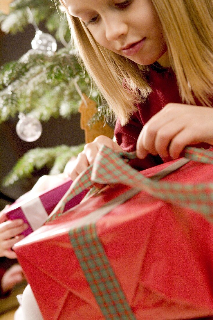 Mädchen öffnet Scheife eines Weihnachtspäckchens