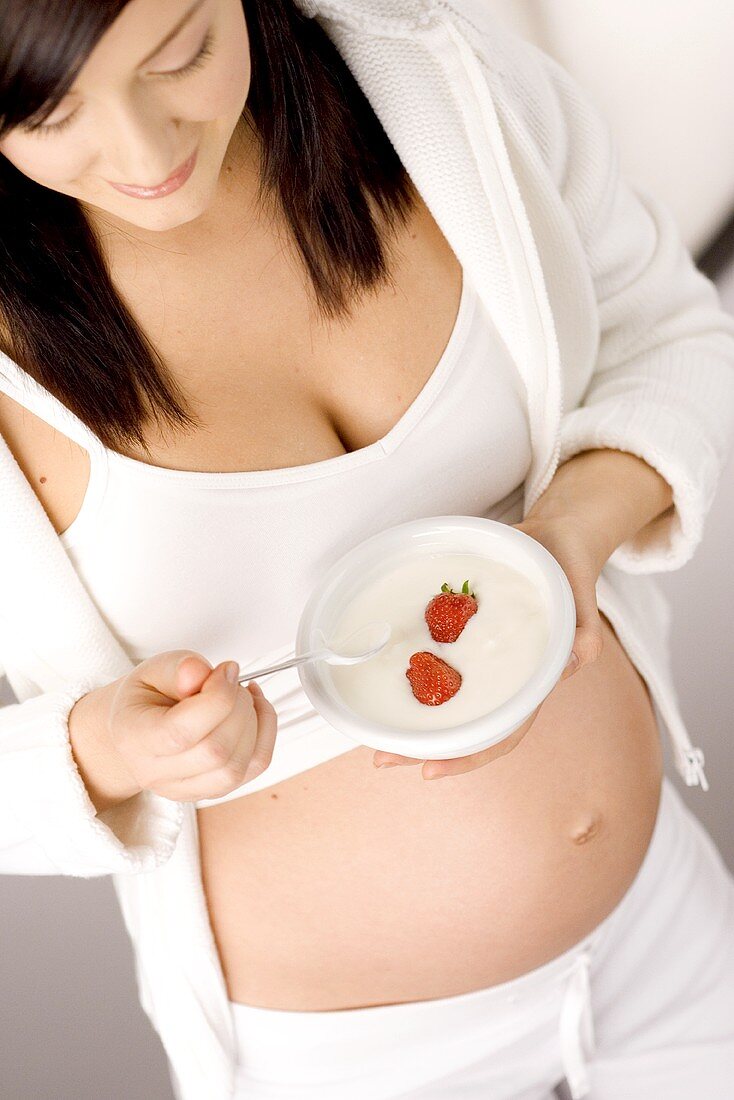 Schwangere Frau hält Schale Naturjoghurt mit Erdbeeren
