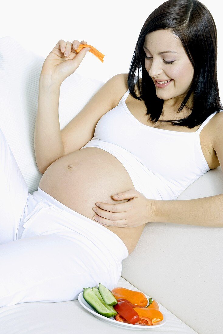 Schwangere Frau auf Sofa liegend, mit Gemüseteller