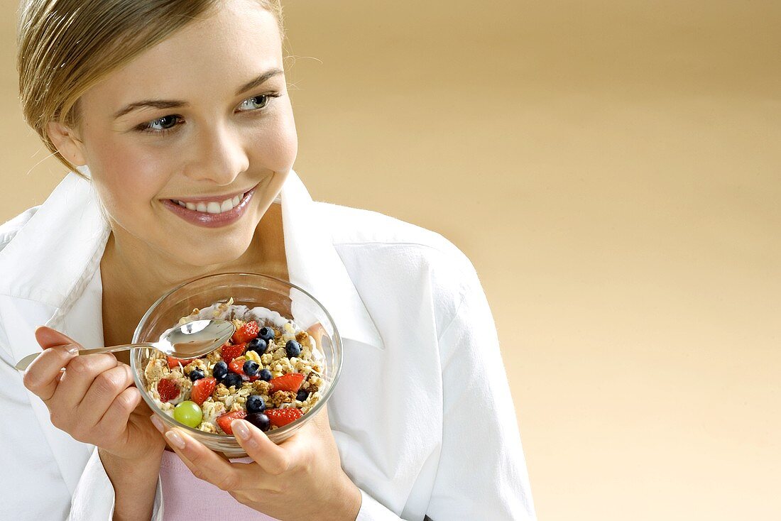 Young woman holding bowl of fruit muesli and spoon