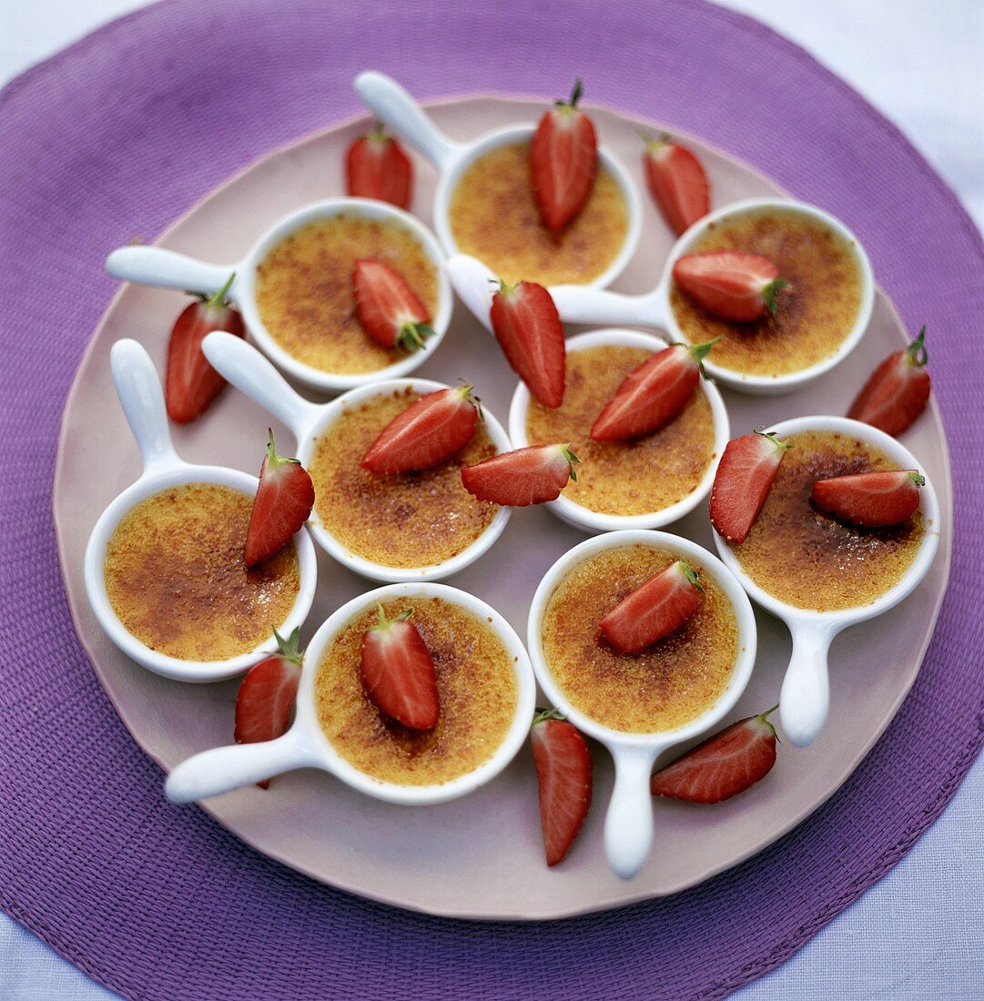 Mehrere Crème brulée in kleinen Förmchen mit Erdbeeren