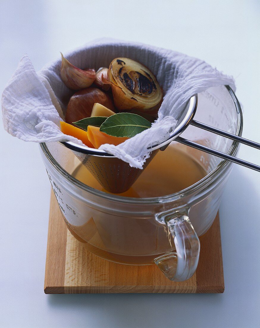 Conical sieve of soup vegetables over clear vegetable broth
