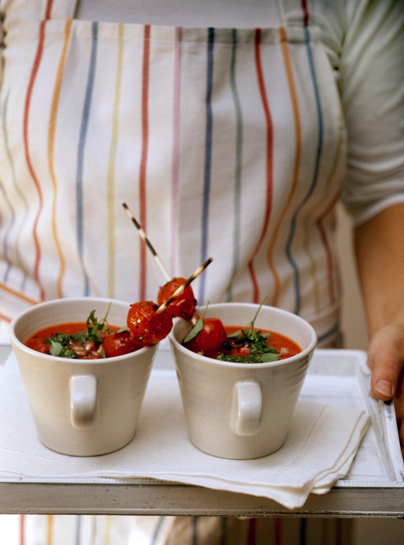 Frau trägt zwei Tassen mit Tomatensuppe auf Tablett