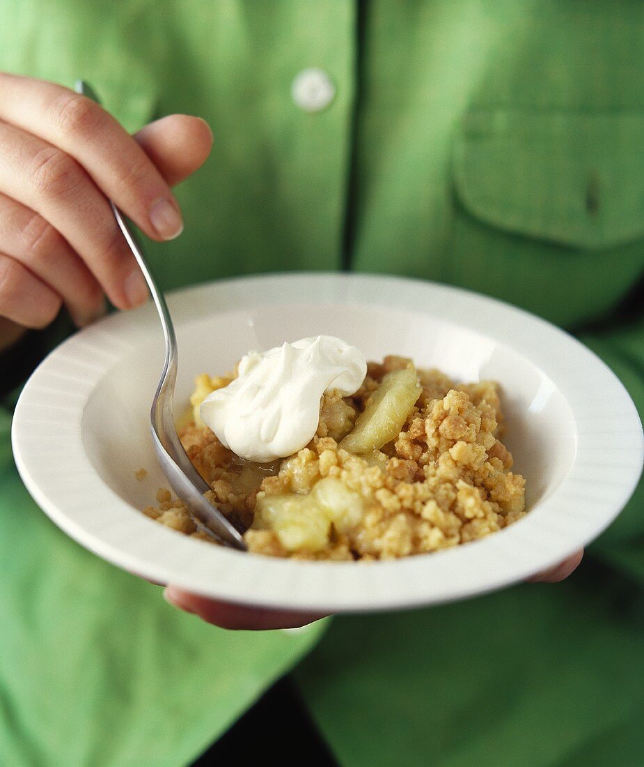 Frau hält Teller mit Apfel-Crumble und Sahne