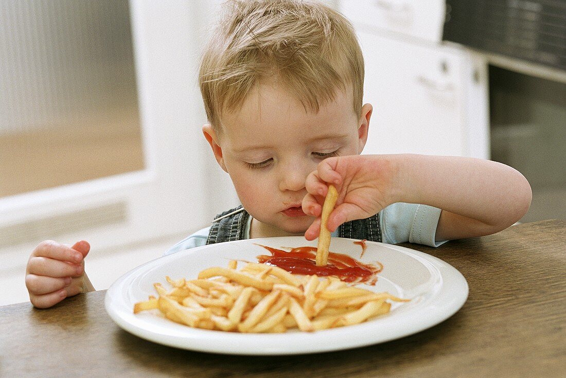 Kleiner Junge Pommes in Ketchup tauchend