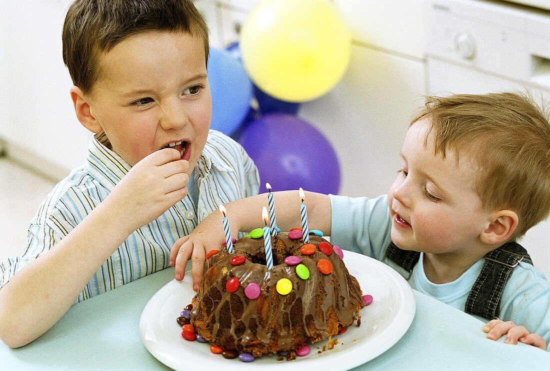 Two boys eating Smarties from birthday cake