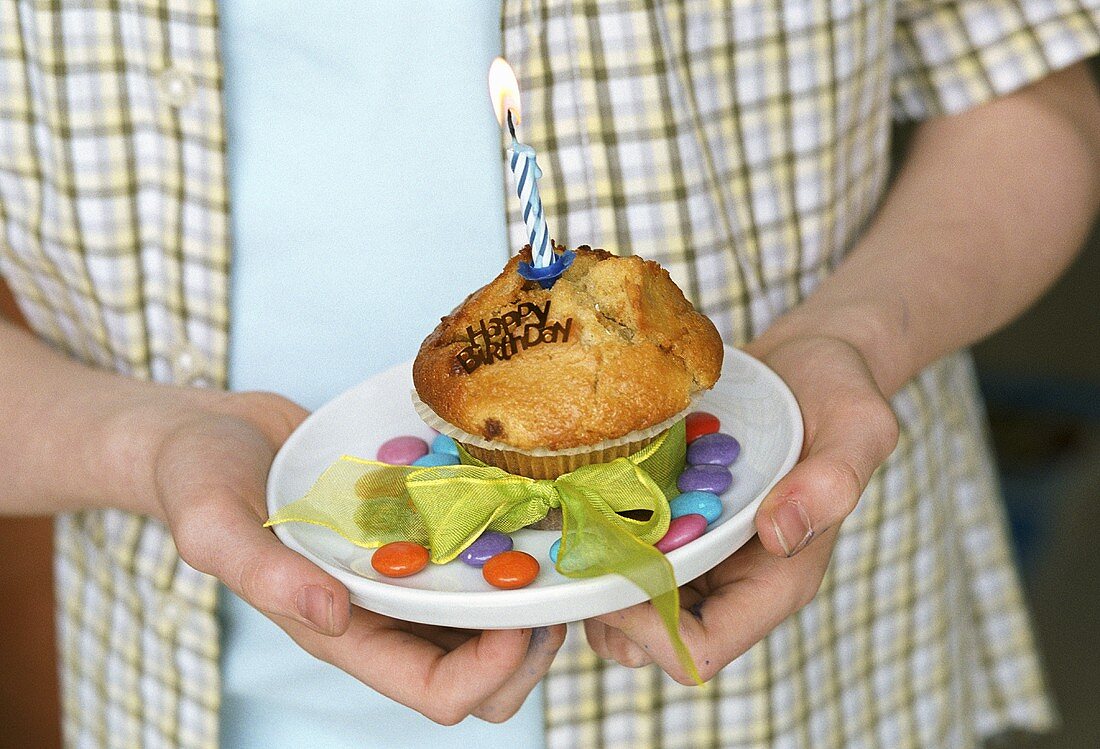 Junge hält Muffin mit brenneder Geburtstagskerze