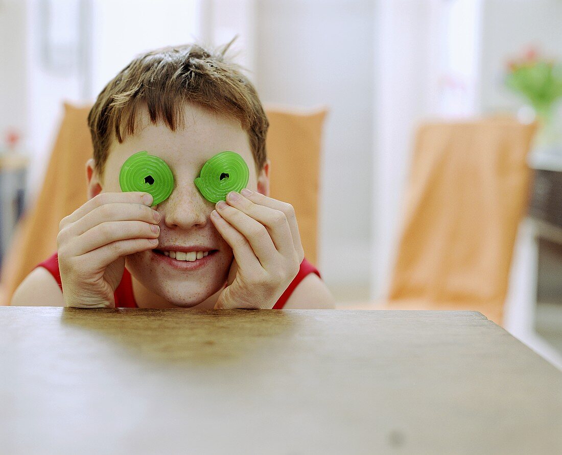 Boy holding green coiled jelly sweets in front of his eyes