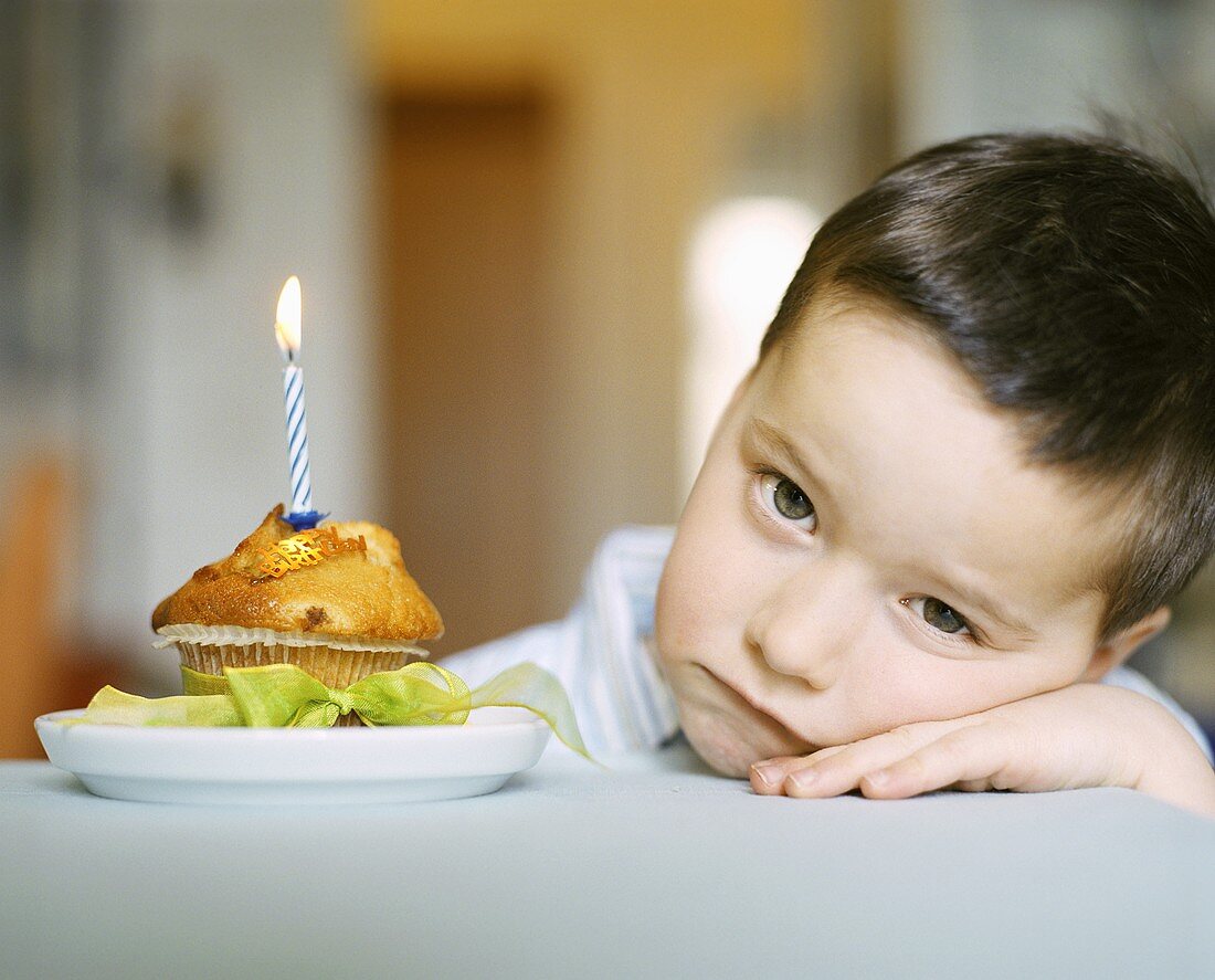 Small boy sitting sadly beside muffin with birthday candle