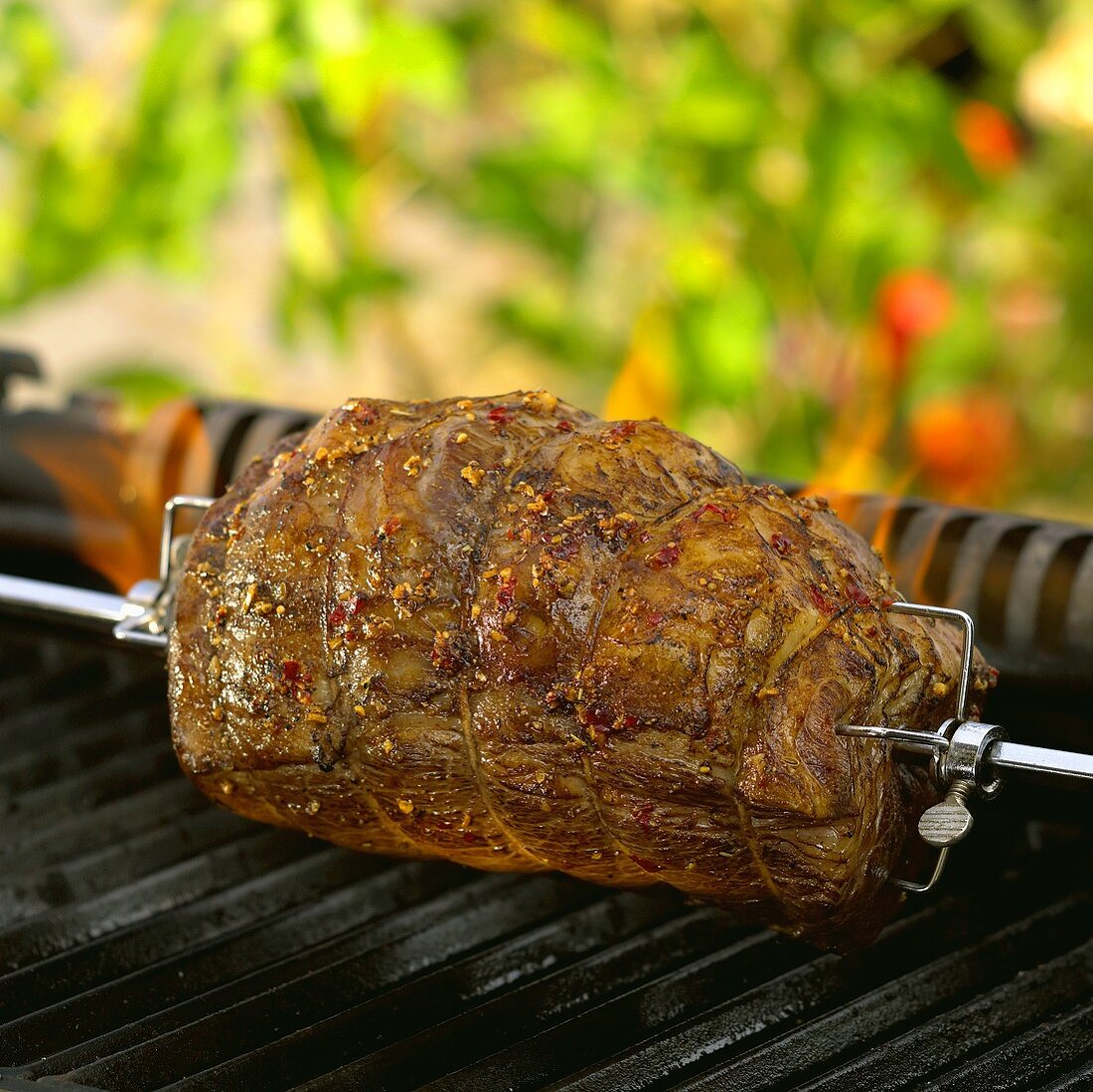 Rolled beef joint on grill spit over barbecue