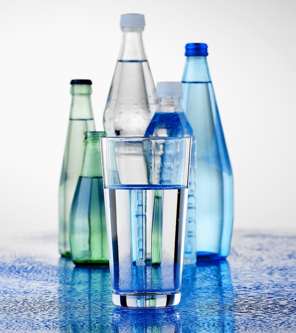 A glass in front of mineral water bottles