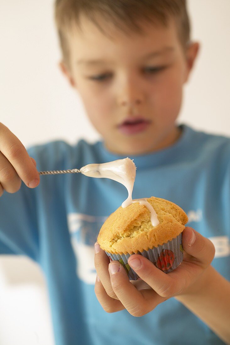 Junge bepinselt Muffin mit Zuckerglasur