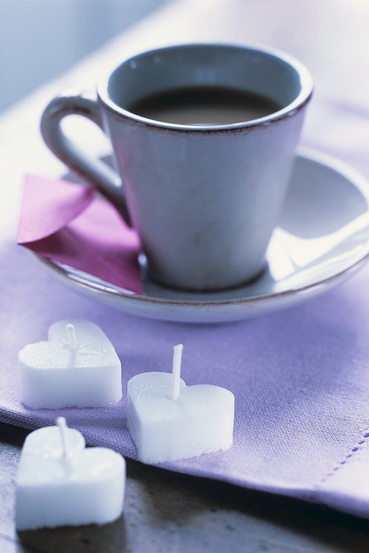 Eine Tasse Kaffee und drei herzförmige Kerzen