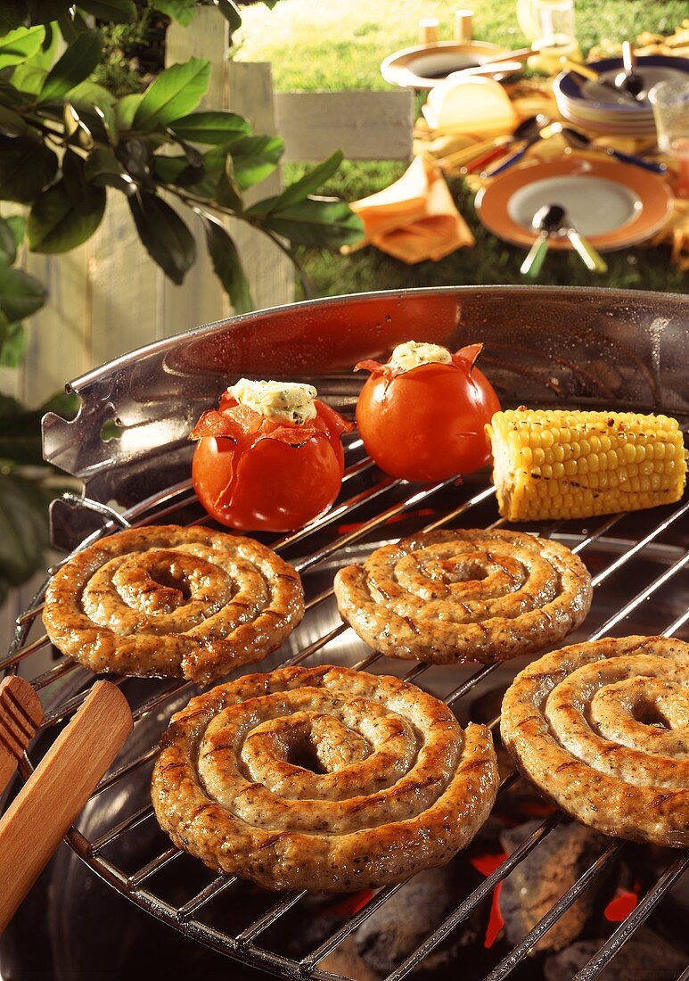 Sausage coils, tomatoes and sweetcorn on a barbecue