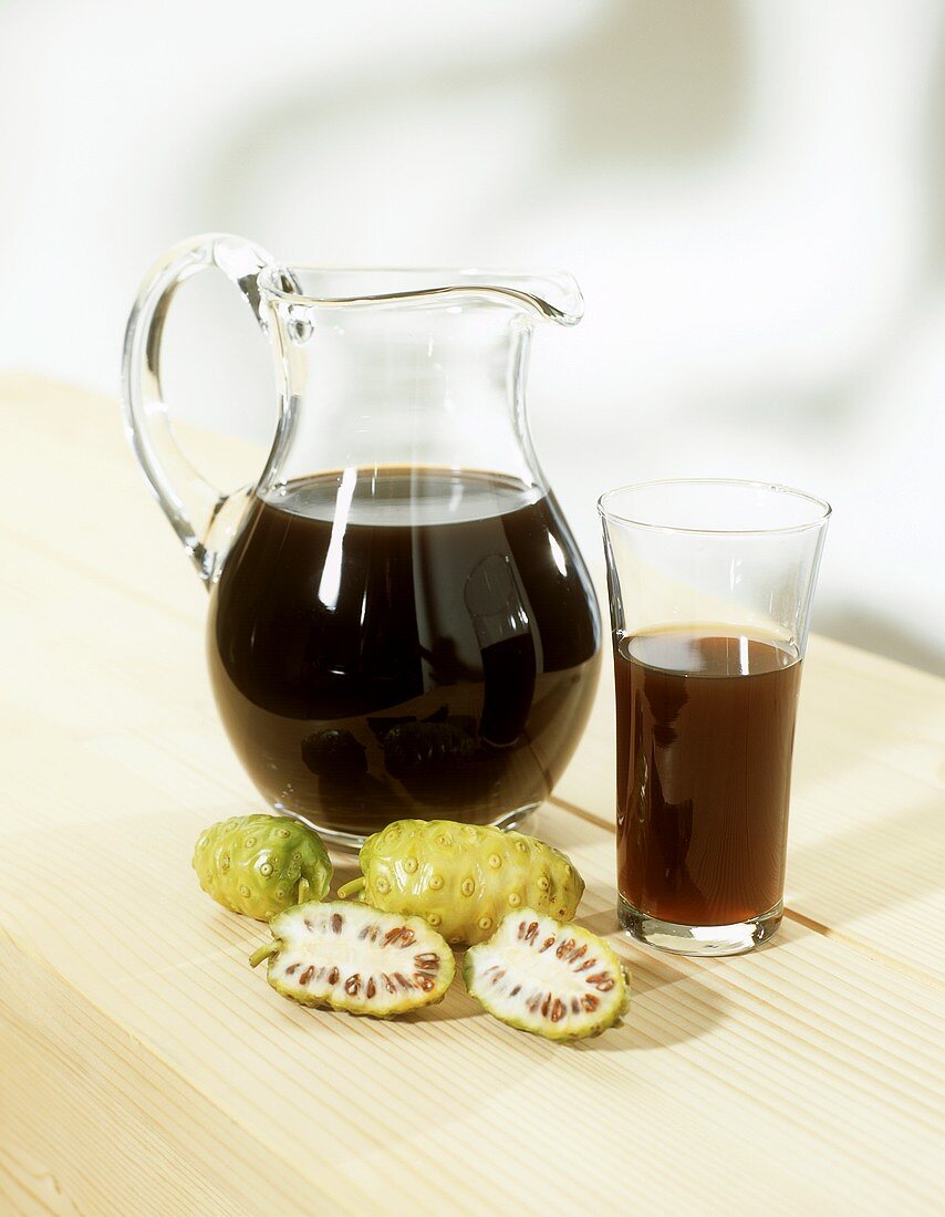 Noni juice in carafe and glass, noni fruits in front