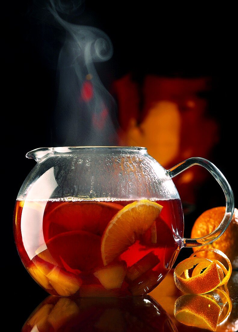 Steaming red wine punch with pieces of fruit in glass teapot