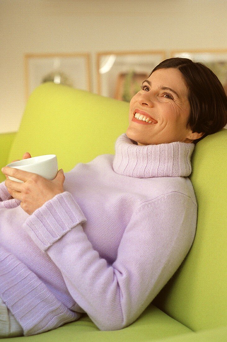 Young woman on sofa with tea or coffee cup (grainy effect)