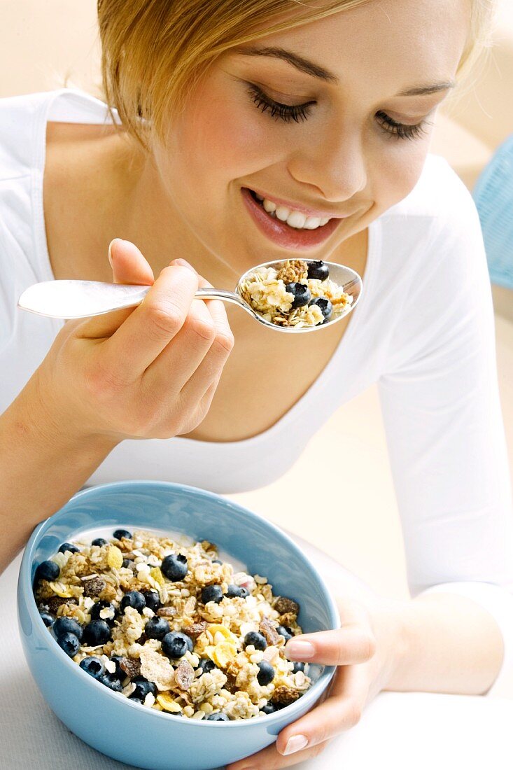 Young woman eating muesli with blueberries