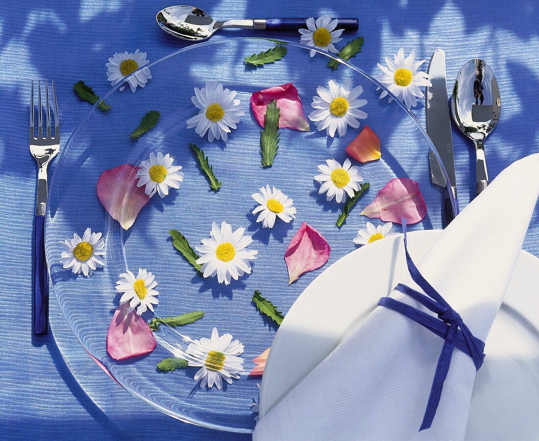 Marguerites & rose petals under place-setting with glass plate