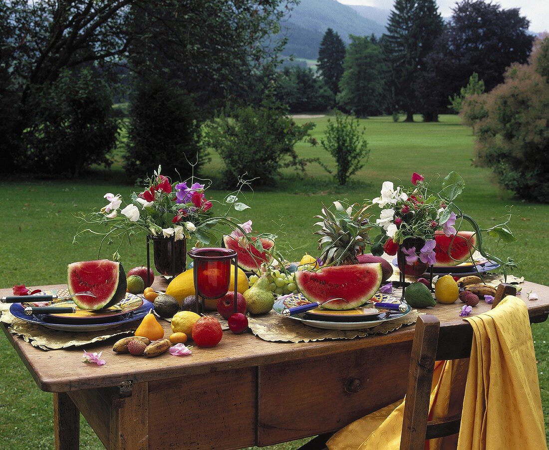 Sommerlich gedeckter Tisch mit Melonen, Früchten und Blumen