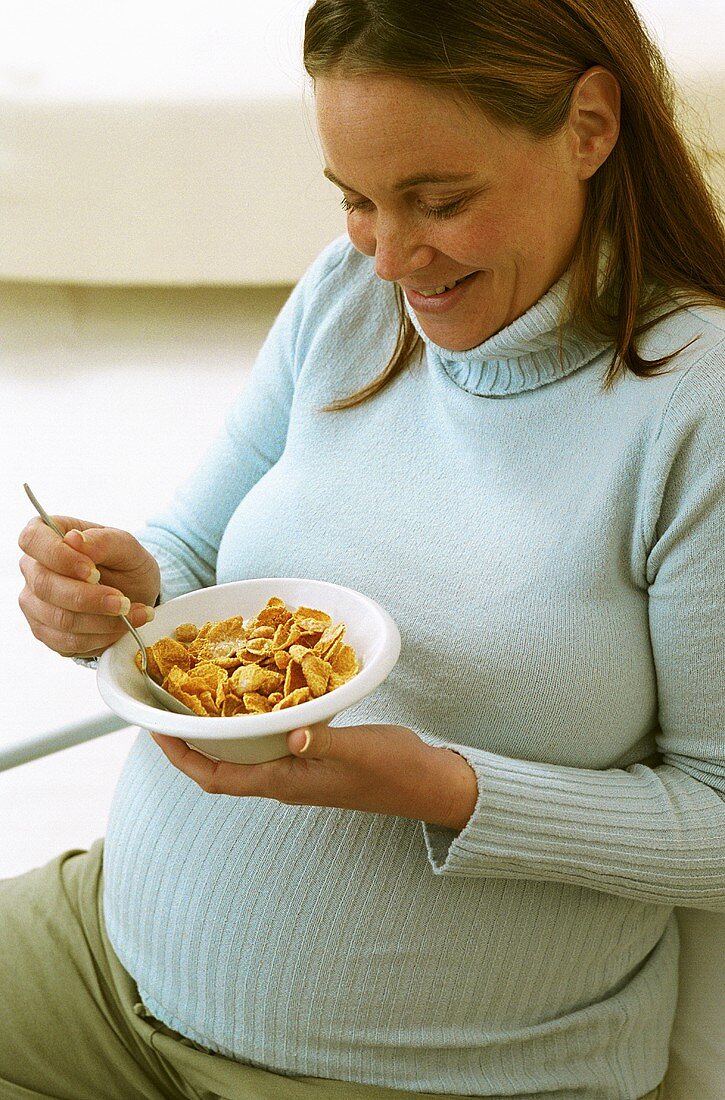 Schwangere Frau isst Schälchen Cornflakes