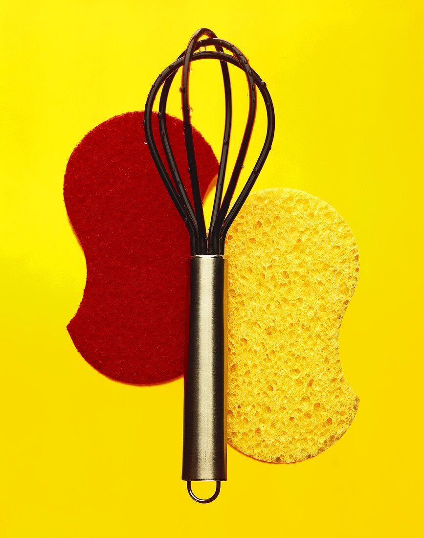 Kitchen sponges and a whisk on yellow background
