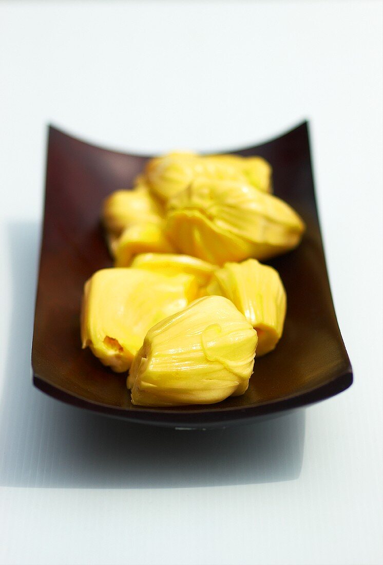 Several segments of a jackfruit in a wooden bowl