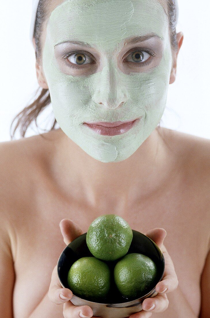 Frau mit Gesichtsmaske hält drei Limetten