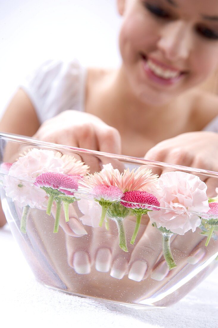 Junge Frau badet die Hände in einer Wasserschüssel mit Blumen