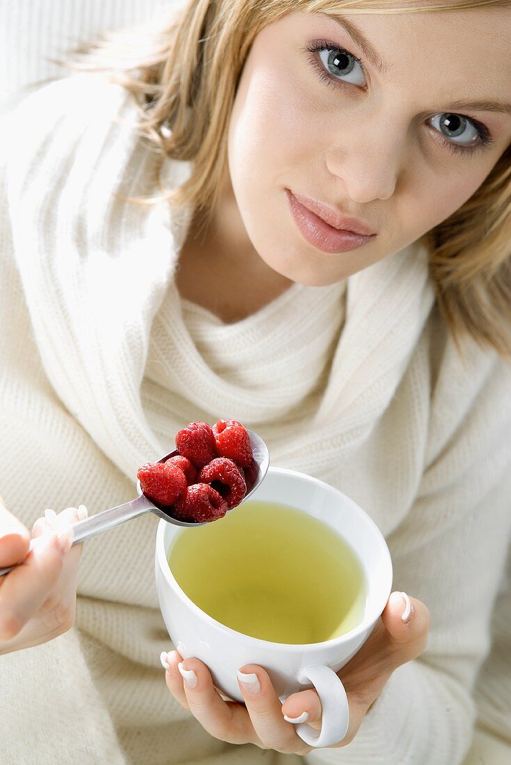 Junge Frau mit einem Löffel Himbeeren und einer Tasse Tee