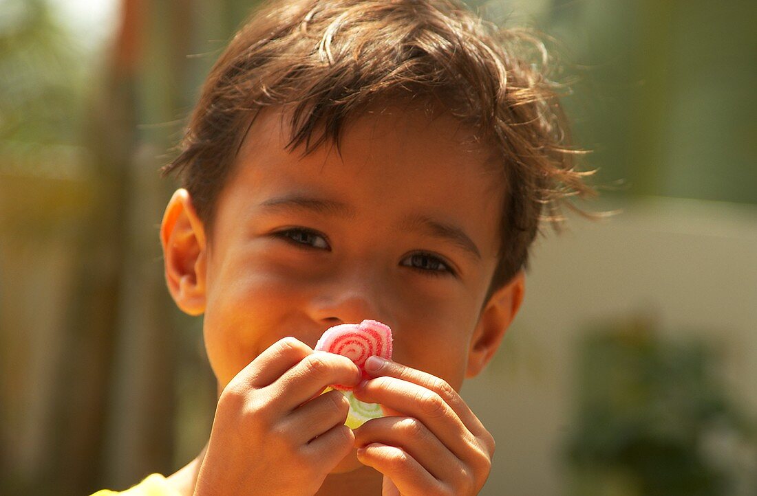 Kleiner indonesischer Junge hält sich Süssigkeit vors Gesicht