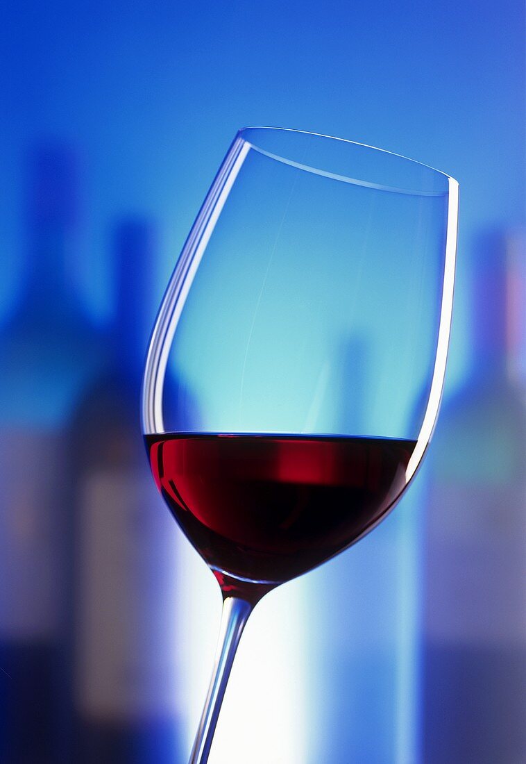A glass of red wine with bottles in the background